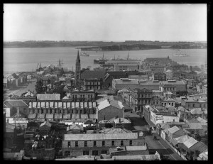 Looking north from St Matthews Church over the city and harbour to Stanley Point showing Hobson Street (extreme left), Hobson Wharf, Chapel Street (Federal Street, right) with St Patricks Cathedral (centre) and premises of Alexandra Hotel (centre) Aurora Hotel, J H Hannon and Charlie Tiy (right) in Albert Street - Sir George Grey Special Collection.